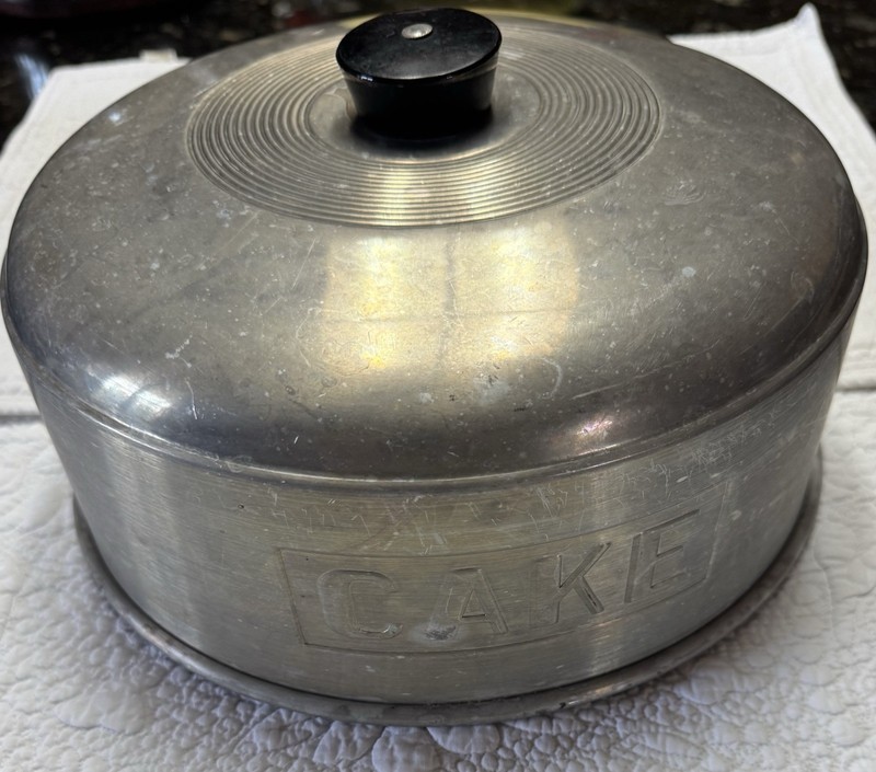 vintage 1950s aluminum cake topper that says in embossed letters “CAKE”