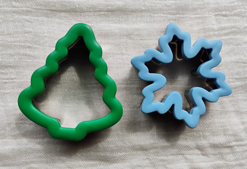 Two Wilton comfort-grip cookie cutters, blue snowflake and green Christmas tree.
